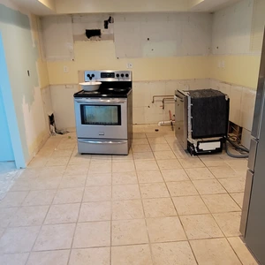 Empty kitchen space after full cabinet removal, with original tile backsplash and flooring exposed