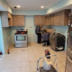 New light-stained maple base and upper cabinets being installed using a laser level for precision alignment