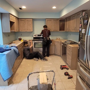 Two-person installation crew fitting upper cabinet runs alongside the existing range
